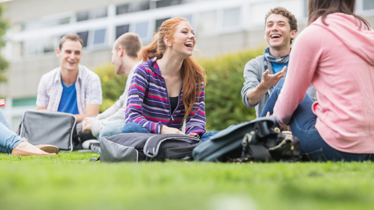 A group of university students sitting on the grass and laughing
