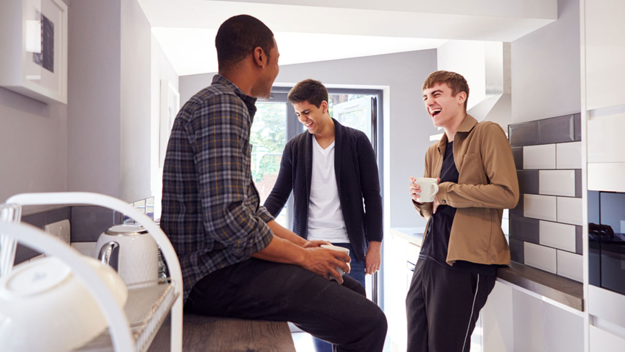 Three friends chatting in a kitchen with one sitting on the countertop