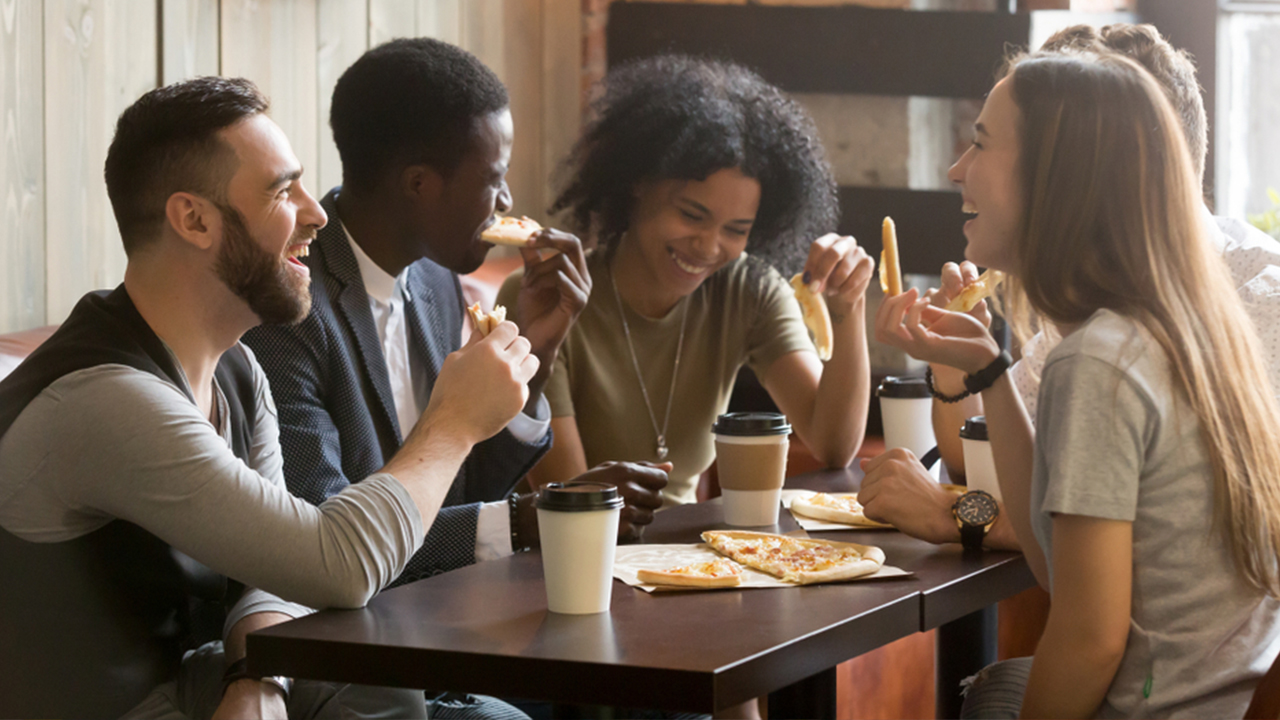 Young people laughing around a table while eating pizza