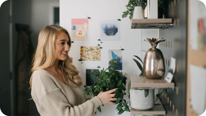 A girl puts a plant on her shelf in a student room