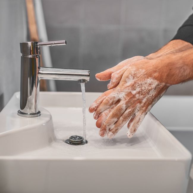 Two hands washing in a bathroom sink 