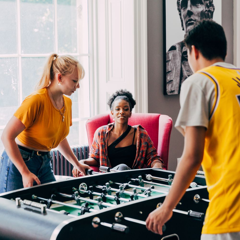 Two students watching two students play foosball